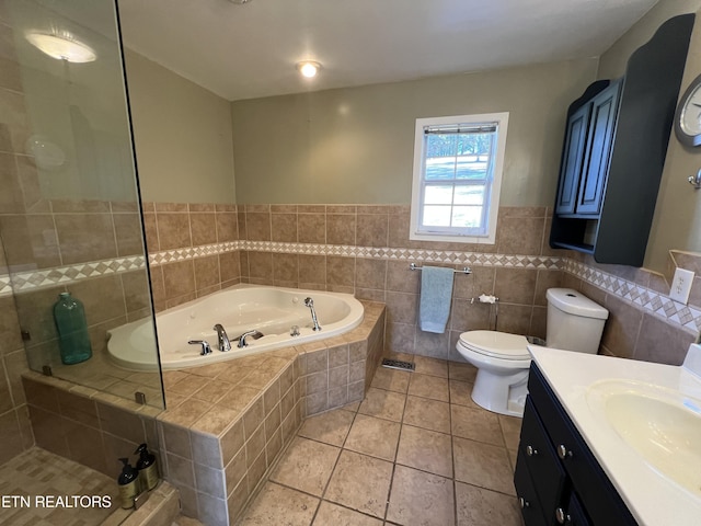 bathroom with tile walls, vanity, tiled bath, tile patterned floors, and toilet