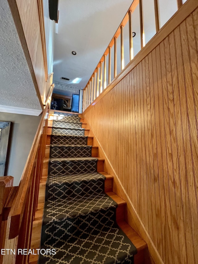 stairs featuring ornamental molding and wood walls