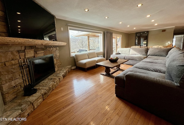 living room with crown molding, a stone fireplace, a textured ceiling, and light wood-type flooring