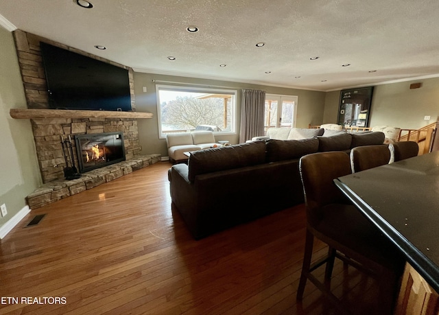 living room with crown molding, wood-type flooring, a fireplace, and a textured ceiling