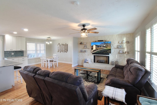 living room featuring ceiling fan, a fireplace, light hardwood / wood-style flooring, and a textured ceiling