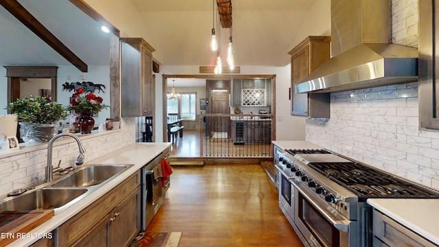 kitchen with sink, decorative light fixtures, beam ceiling, range with two ovens, and wall chimney range hood