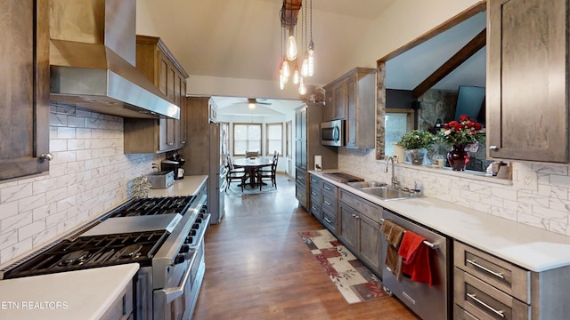 kitchen with sink, hanging light fixtures, ceiling fan, stainless steel appliances, and wall chimney range hood