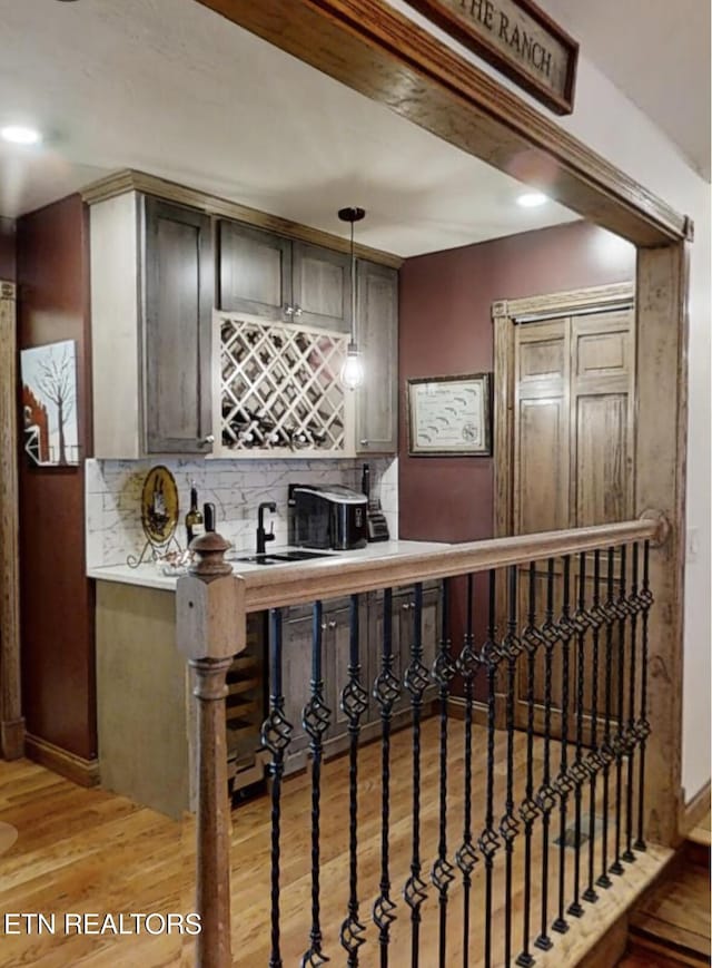 bar with decorative light fixtures, sink, light hardwood / wood-style flooring, and backsplash