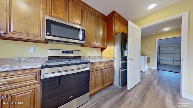 kitchen with light stone countertops, appliances with stainless steel finishes, and light wood-type flooring