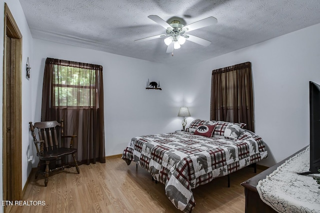 bedroom with ceiling fan, a textured ceiling, and light hardwood / wood-style floors