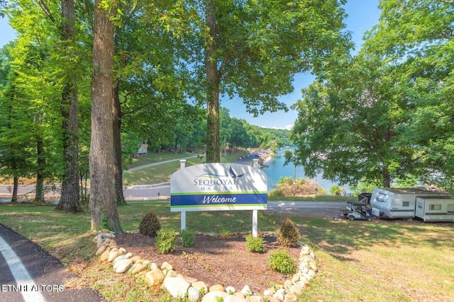 community / neighborhood sign featuring a water view and a lawn