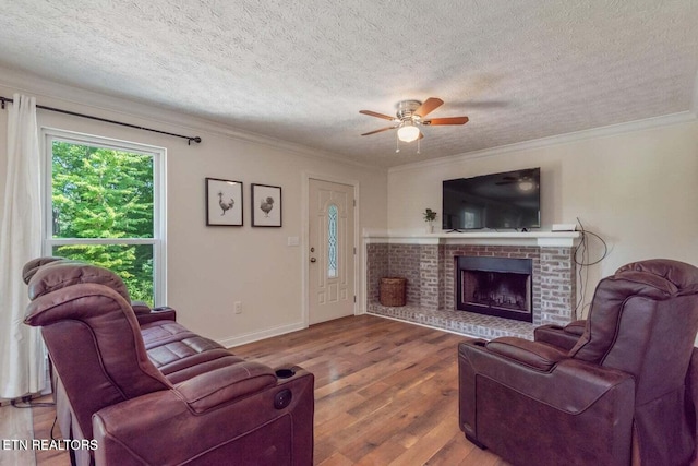 living room featuring ceiling fan, a fireplace, crown molding, hardwood / wood-style flooring, and a textured ceiling