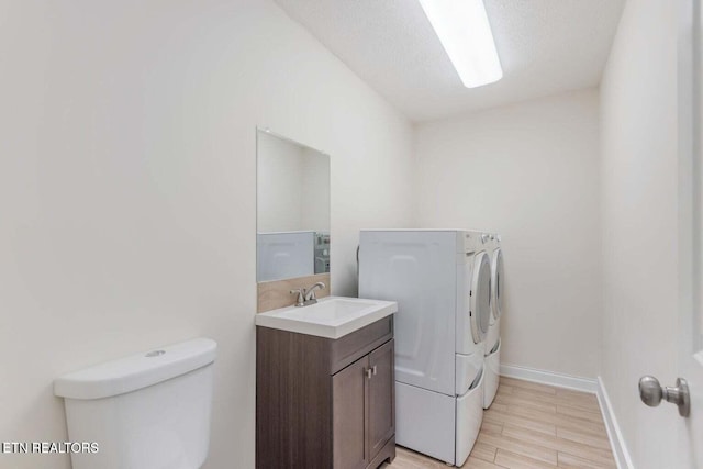 clothes washing area with sink, washer and dryer, a textured ceiling, and light hardwood / wood-style flooring