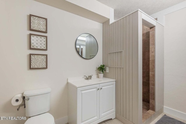 bathroom with a textured ceiling, toilet, vanity, and a tile shower