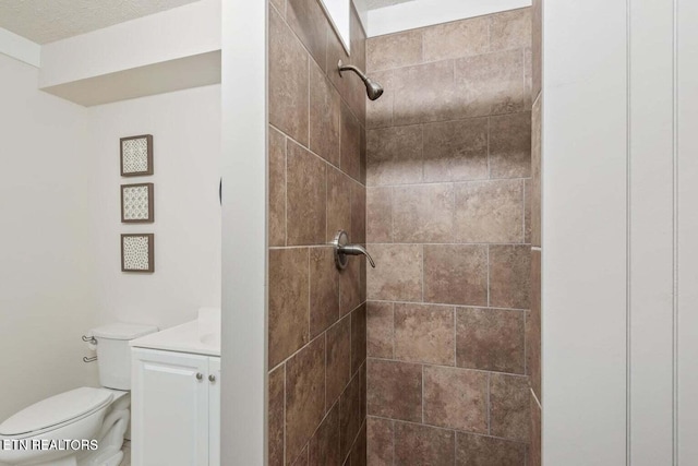 bathroom featuring toilet, vanity, tiled shower, and a textured ceiling