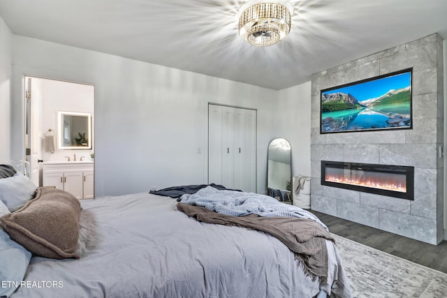 bedroom with dark wood-type flooring, ensuite bathroom, a tile fireplace, and a closet