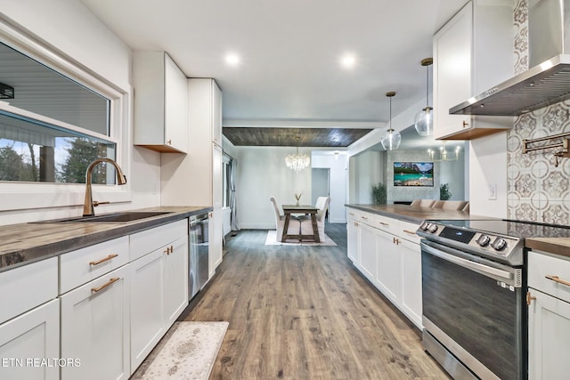 kitchen with white cabinetry, appliances with stainless steel finishes, wall chimney range hood, pendant lighting, and sink