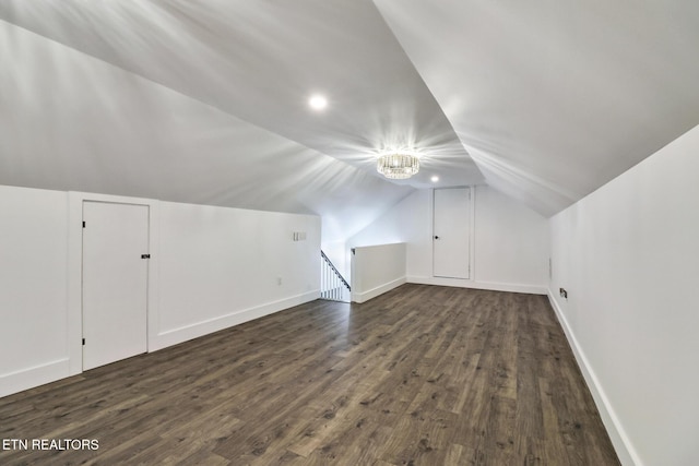 additional living space featuring vaulted ceiling, dark wood-type flooring, and a notable chandelier