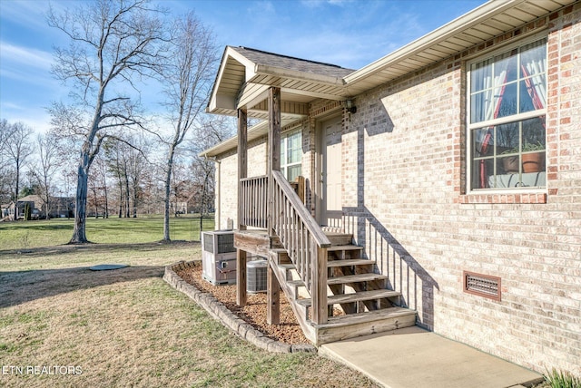 entrance to property featuring crawl space, brick siding, a lawn, and central AC