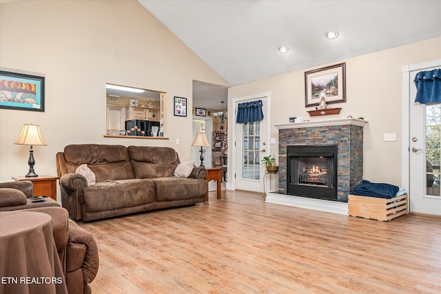 living area with high vaulted ceiling, a stone fireplace, and light wood-type flooring