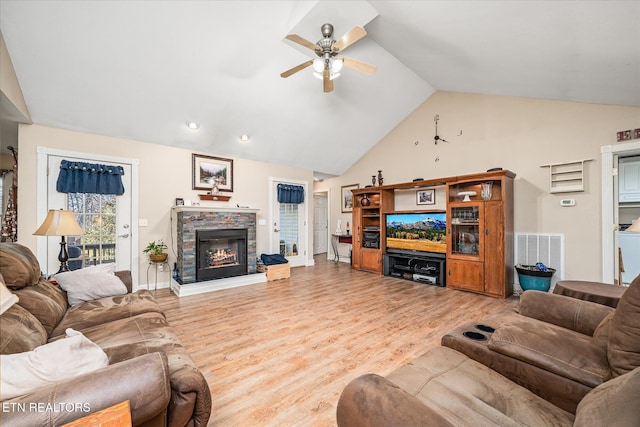 living area with lofted ceiling, a stone fireplace, visible vents, and light wood-style flooring