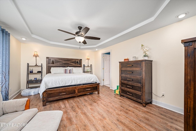 bedroom with a ceiling fan, light wood-style flooring, a tray ceiling, and baseboards