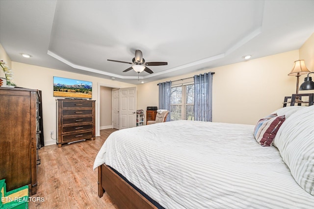 bedroom featuring light wood-type flooring, a raised ceiling, ceiling fan, and baseboards