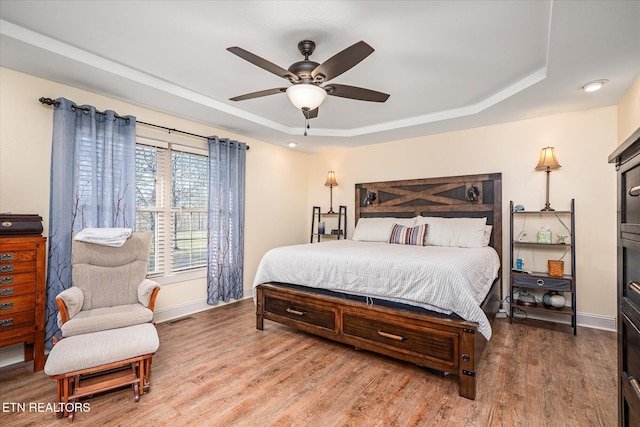 bedroom featuring a tray ceiling, wood finished floors, visible vents, and baseboards