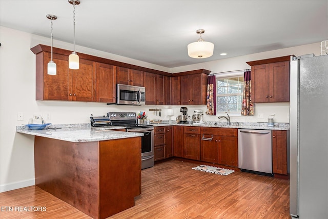 kitchen with stainless steel appliances, pendant lighting, a peninsula, and light wood finished floors