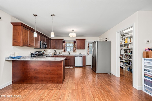 kitchen with a peninsula, hanging light fixtures, appliances with stainless steel finishes, light stone countertops, and light wood finished floors