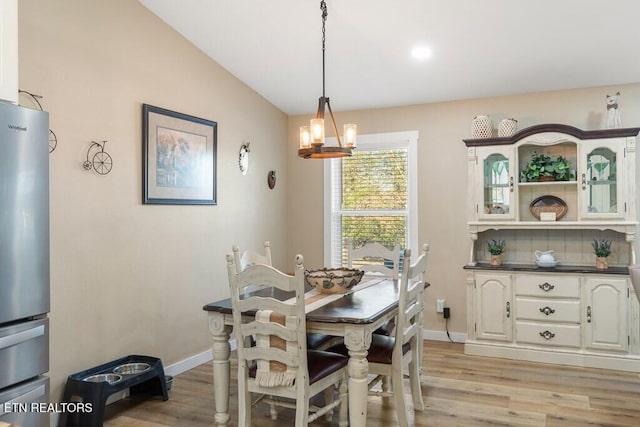 dining space with light wood-type flooring, vaulted ceiling, and a notable chandelier