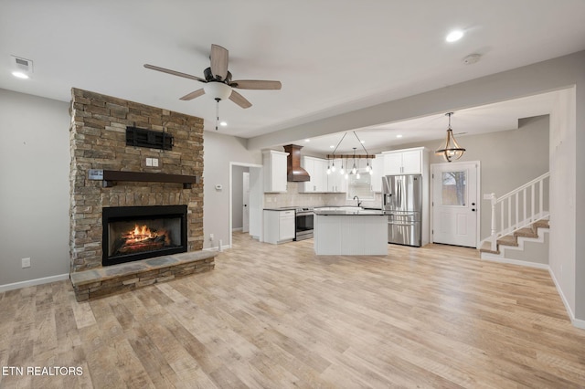 unfurnished living room with ceiling fan, light hardwood / wood-style floors, a stone fireplace, and sink