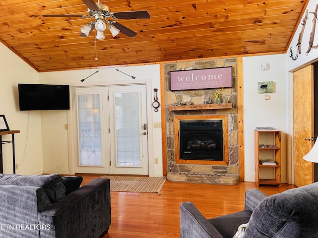 living room with wood ceiling, a stone fireplace, light hardwood / wood-style floors, and vaulted ceiling