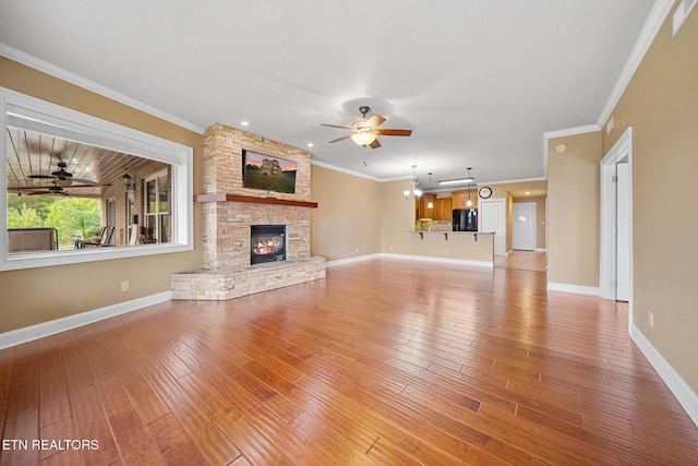 unfurnished living room featuring ceiling fan with notable chandelier, hardwood / wood-style floors, ornamental molding, and a fireplace