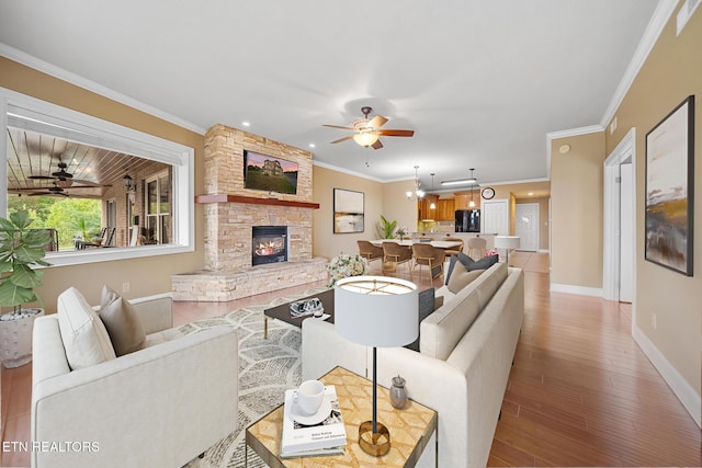 living room with crown molding, ceiling fan with notable chandelier, hardwood / wood-style floors, and a stone fireplace