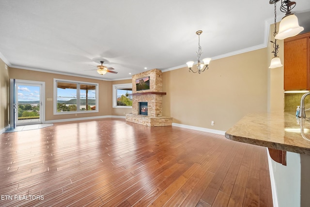 unfurnished living room with a fireplace, ceiling fan with notable chandelier, ornamental molding, and hardwood / wood-style floors