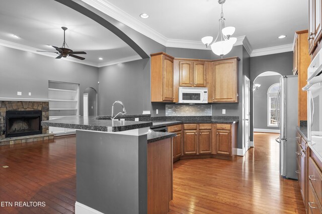 kitchen with ceiling fan, arched walkways, freestanding refrigerator, a peninsula, and white microwave