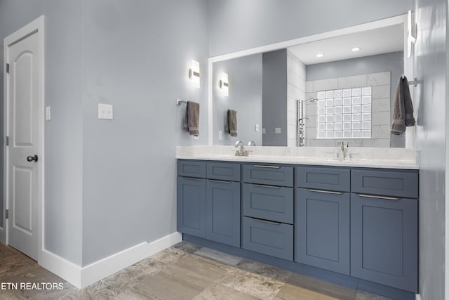 full bathroom featuring a sink, baseboards, a tile shower, and double vanity