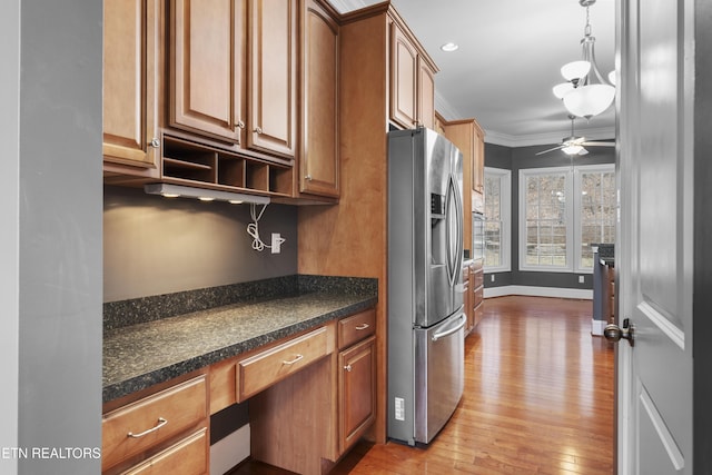 kitchen featuring dark countertops, built in desk, a ceiling fan, wood finished floors, and stainless steel refrigerator with ice dispenser