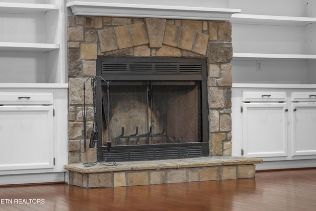 interior details with built in features, a stone fireplace, and wood finished floors