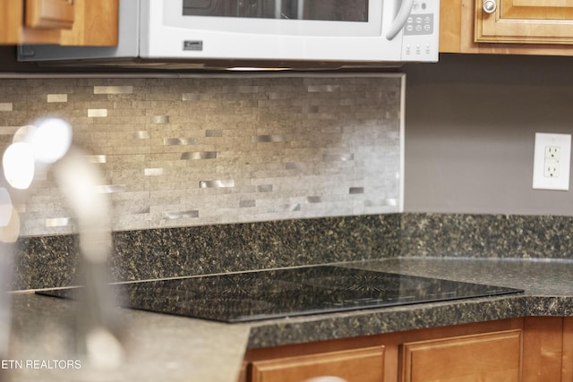interior details featuring brown cabinetry, dark countertops, tasteful backsplash, white microwave, and black electric stovetop