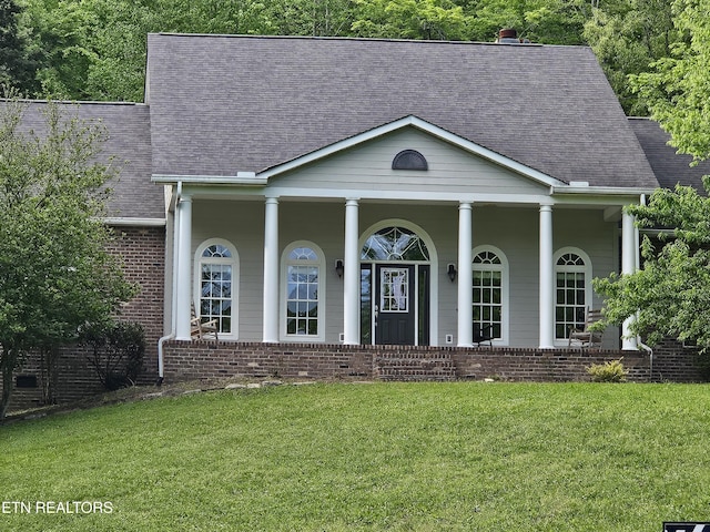 neoclassical home with roof with shingles, covered porch, brick siding, and a front yard