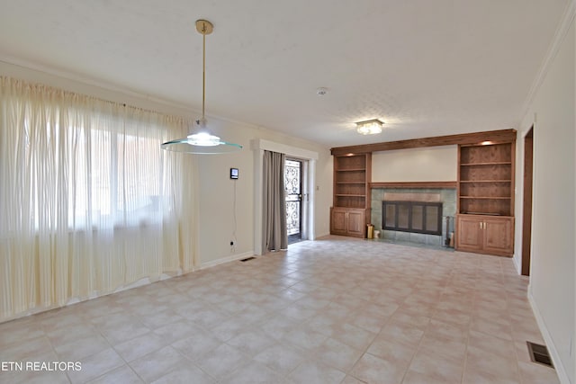 unfurnished living room featuring a tiled fireplace, built in shelves, visible vents, and ornamental molding