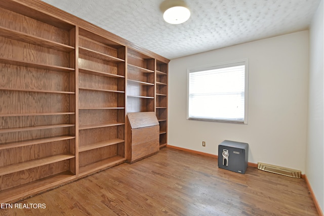 interior space with visible vents, a textured ceiling, baseboards, and wood finished floors