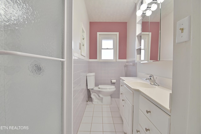 bathroom with vanity, a stall shower, tile patterned floors, toilet, and tile walls