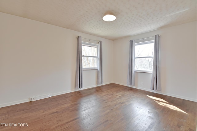 unfurnished room with plenty of natural light, wood finished floors, and baseboards