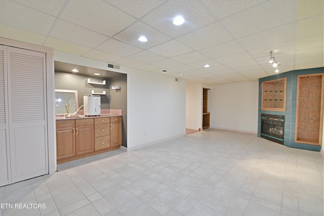 unfurnished living room with visible vents, baseboards, a tiled fireplace, a drop ceiling, and a sink