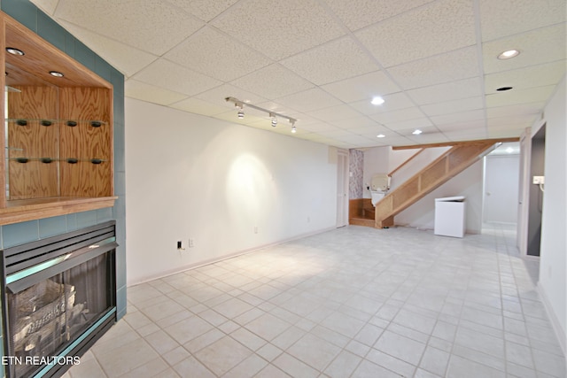 finished below grade area with recessed lighting, stairway, baseboards, a fireplace, and a paneled ceiling