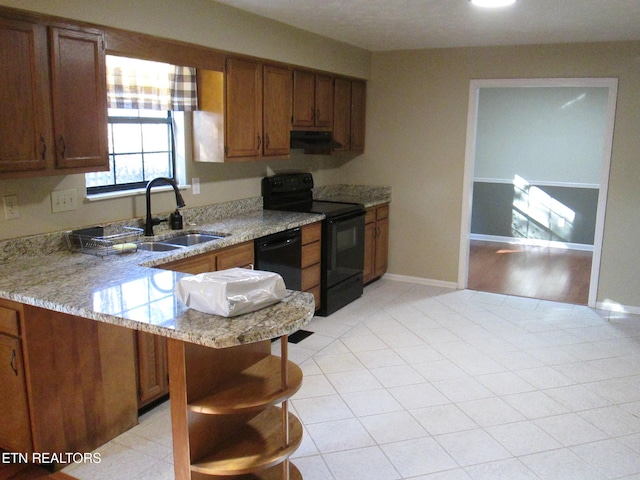 kitchen with black appliances, sink, kitchen peninsula, light stone counters, and a breakfast bar area