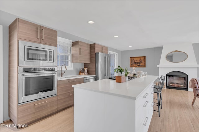 kitchen with sink, a breakfast bar area, a center island, stainless steel appliances, and light wood-type flooring