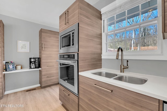 kitchen with appliances with stainless steel finishes, sink, and light wood-type flooring