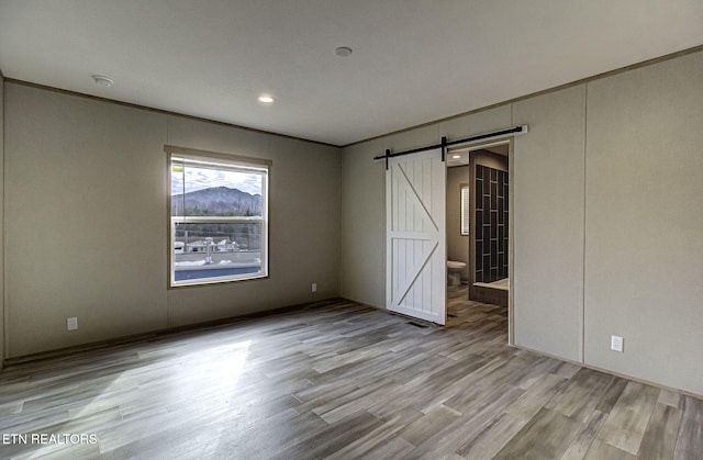 spare room featuring crown molding, a barn door, and light hardwood / wood-style flooring