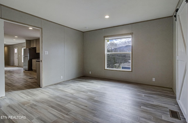 empty room with crown molding, a barn door, and light hardwood / wood-style flooring