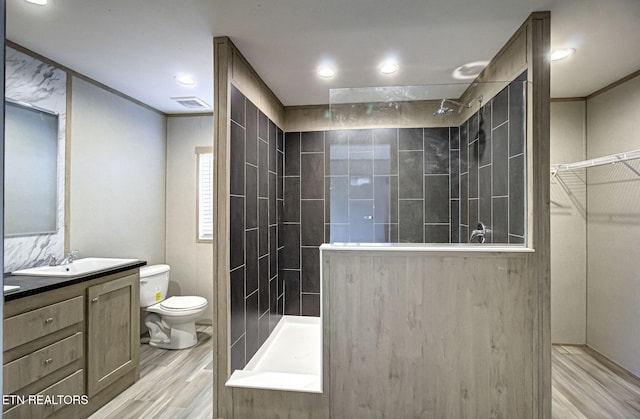 bathroom with a tile shower, vanity, hardwood / wood-style flooring, and toilet